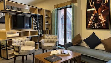 A modern living room with a sofa, two armchairs, a coffee table with a book, a TV, and a bookshelf.