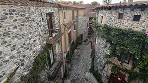 Un stretto vicolo in pietra tra edifici tradizionali in pietra con tetti in terracotta, una scala in pietra e un piccolo cortile con una fontana.
