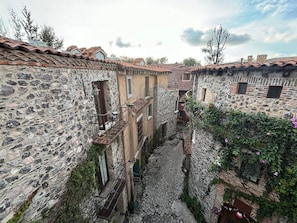 A narrow stone alleyway between traditional stone buildings with terracotta roofs, a stone staircase, and a small courtyard with a fountain. - Castello di Carlo – Loft Carlo II. (Val'Quirico)
