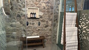 Un bagno con parete in pietra, una panca di legno, uno scaffale con articoli da toilette e un porta asciugamani con asciugamani.