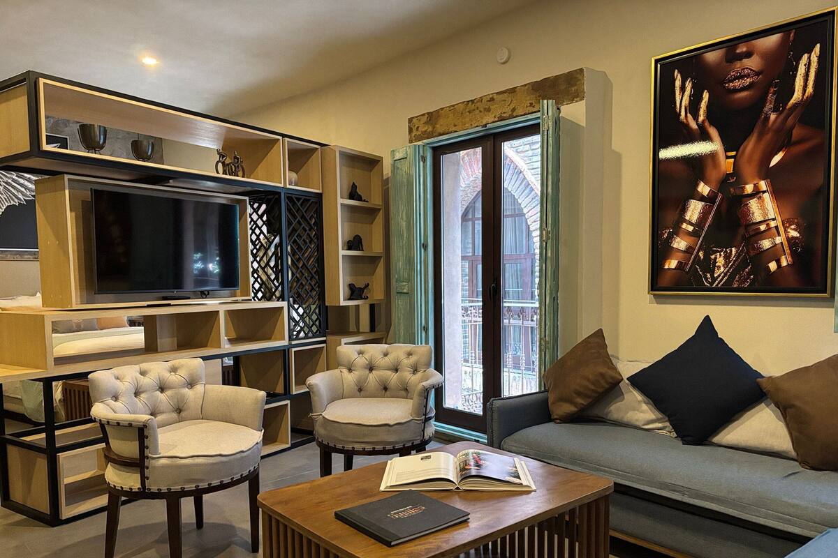 A modern living room with a sofa, two armchairs, a coffee table with a book, a TV, and a bookshelf.