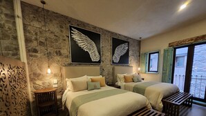 Camera d'albergo con due letti, una parete in pietra e un'opera d'arte raffigurante delle ali.