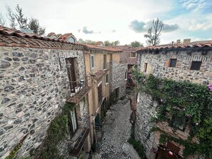 Un estrecho callejón empedrado entre edificios de piedra tradicionales con tejados de teja, una escalera de piedra y un pequeño patio con una fuente.