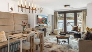 A modern living room with a fireplace, a mounted TV, and a large window with a view of the outdoors. - Auberge Resort 5 Star Residence (Mountain Village)
