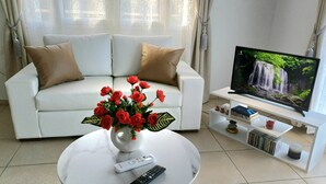 A living room with a white sofa, a vase of red flowers, a remote control, and a TV displaying a waterfall scene.