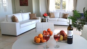 A modern living room with two white sofas, a coffee table with fruit and wine glasses, and a bottle of wine.