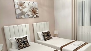 A hotel room with two beds, each with a white bedspread and brown trim, a nightstand with a lamp, and a wall-mounted artwork of flowers.
