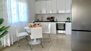 A modern kitchen with white cabinetry, a stainless steel refrigerator, and a dining area with white chairs and a round table.