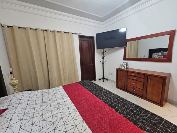 Un dormitorio con cama, televisión, perchero y cómoda de madera.