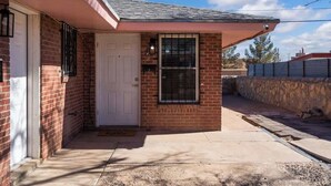 A single-story brick house with a white door, a small window with blinds, and a visible chimney. - Sleek 2-Bed 1-Bath Home • Near Fort Bliss (El Paso)