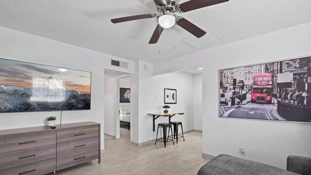 A modern living room with a flat-screen TV, a ceiling fan, a sofa, and a dining area with stools. - Sleek 2-Bed 1-Bath Home • Near Fort Bliss (El Paso)