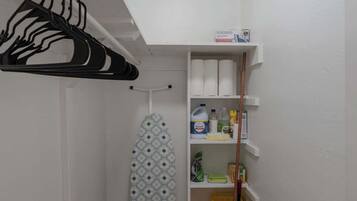 A laundry room with a drying rack, ironing board, shelves with cleaning supplies, and a mop cart.