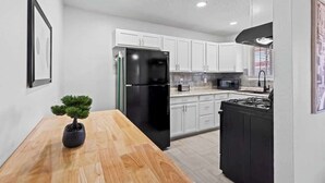 A modern kitchen with white cabinets, a black refrigerator, a microwave, and a stove. - Sleek 2-Bed 1-Bath Home • Near Fort Bliss (El Paso)