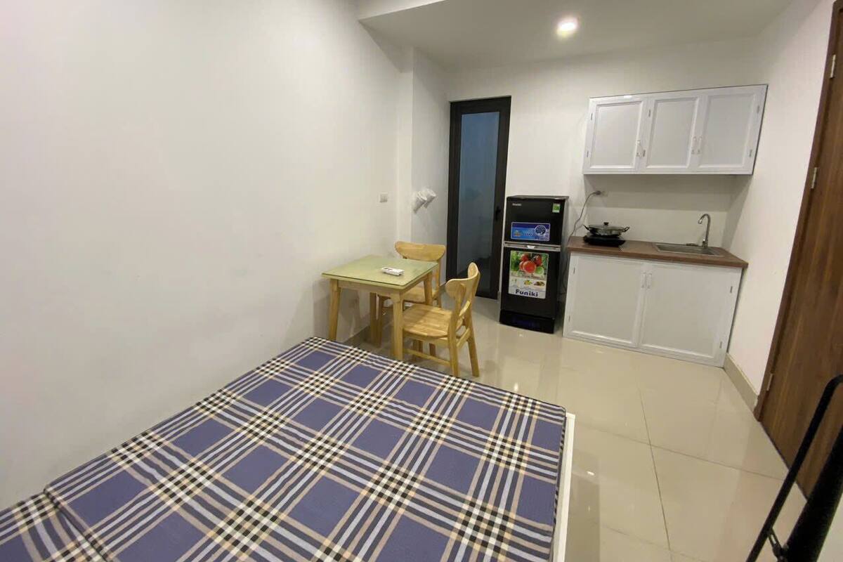 Una habitación pequeña y funcional con cama, una mesa y sillas, kitchenette y una puerta.