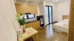 Habitación de hotel compacta con kitchenette, una cama, una mesita con un florero y vistas al balcón exterior.