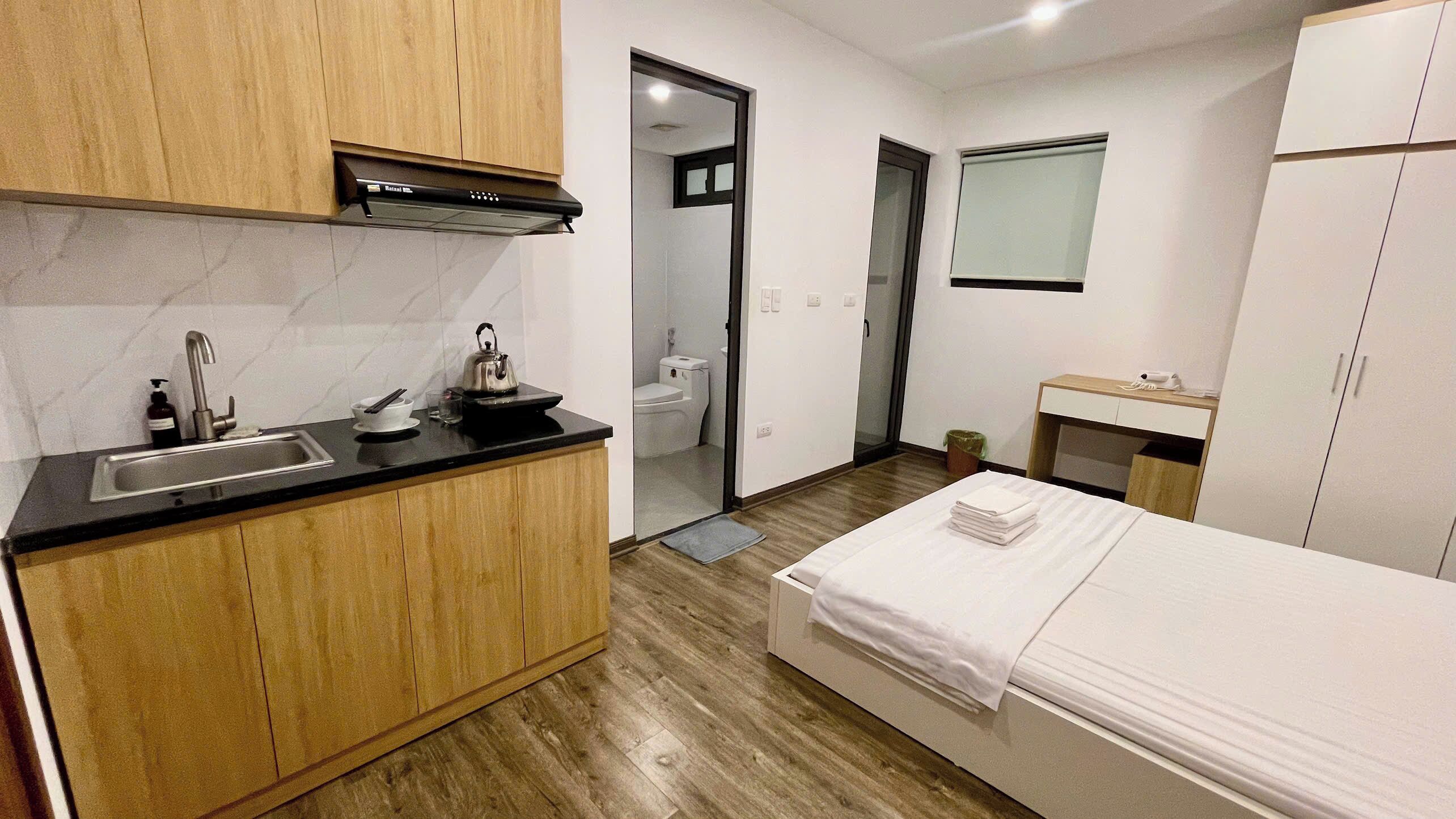 Een compacte hotelkamer met kitchenette, een bed, een kleine badkamer en een spiegel.