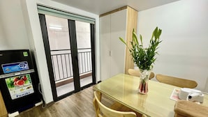 Un pequeño comedor con una mesa de vidrio, sillas de madera, una planta en maceta y un refrigerador con dispensador de bebidas.