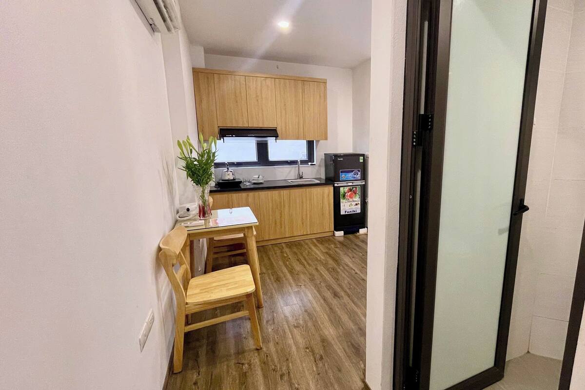 Cocina compacta con armarios de madera, un refrigerador y una pequeña mesa de comedor con una silla.