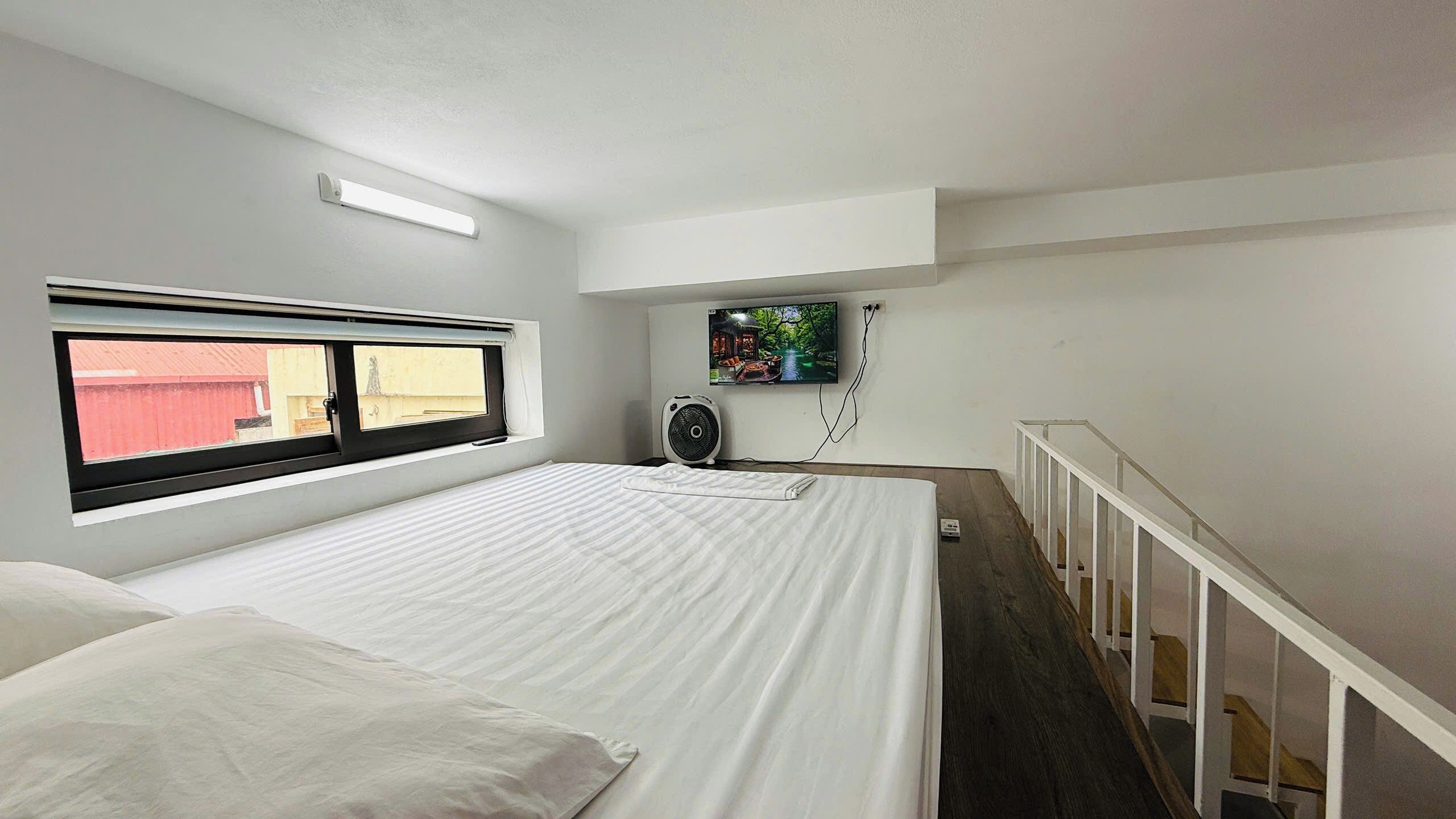 A bedroom with a bed, a window, a TV, and a fan.