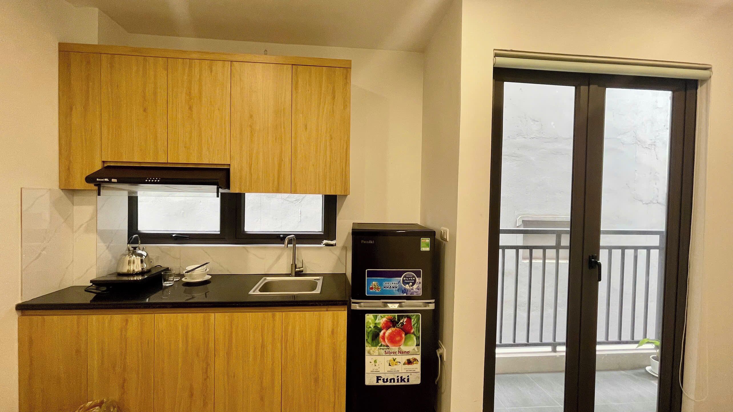 A compact kitchen with wooden cabinets, a black countertop, a kettle, a sink, and a refrigerator with a 'Funiki' sticker.