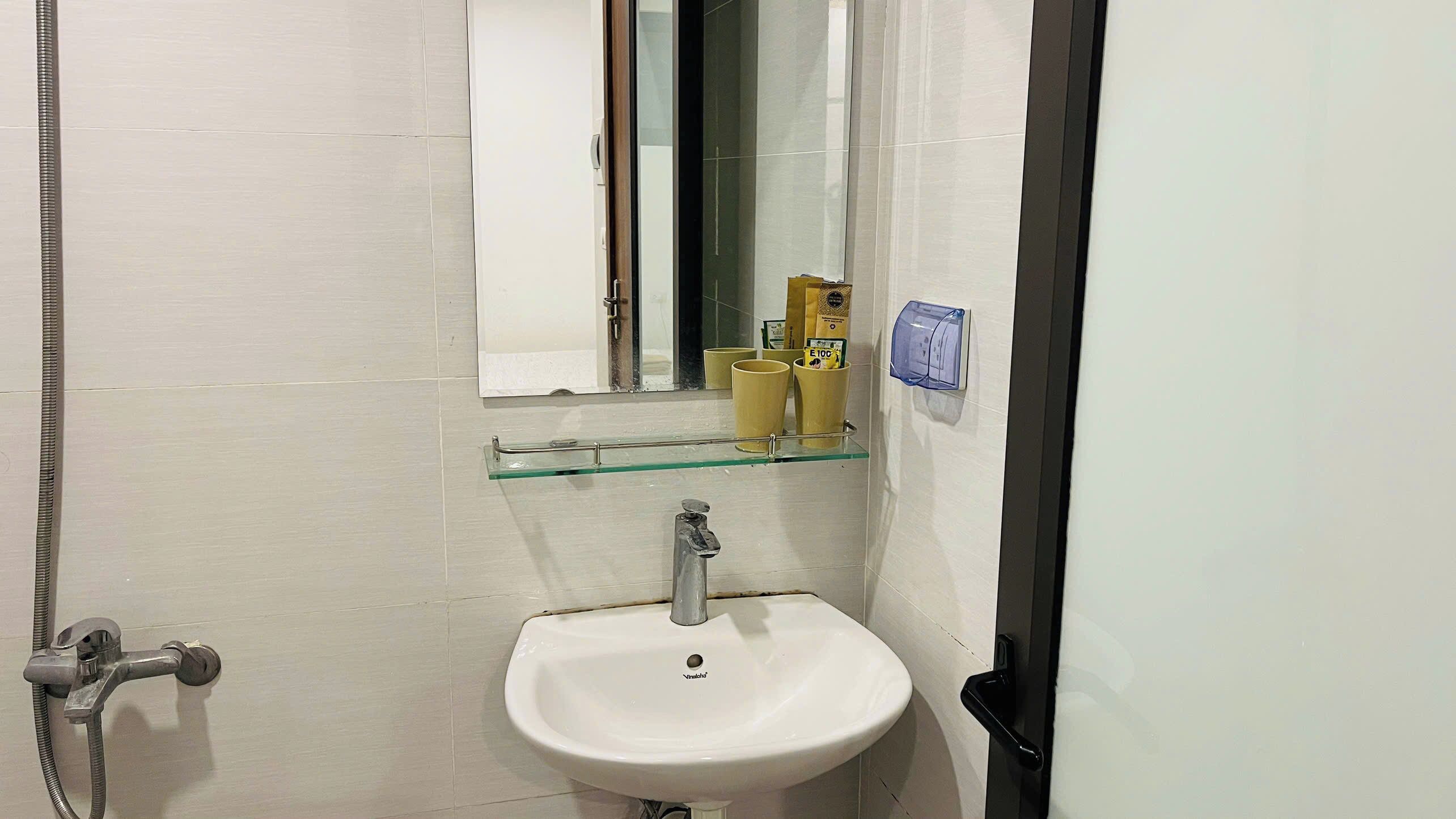Ein Badezimmer mit einem weißen Waschbecken, einer Glasablage, einem Spiegel und einer Dusche.