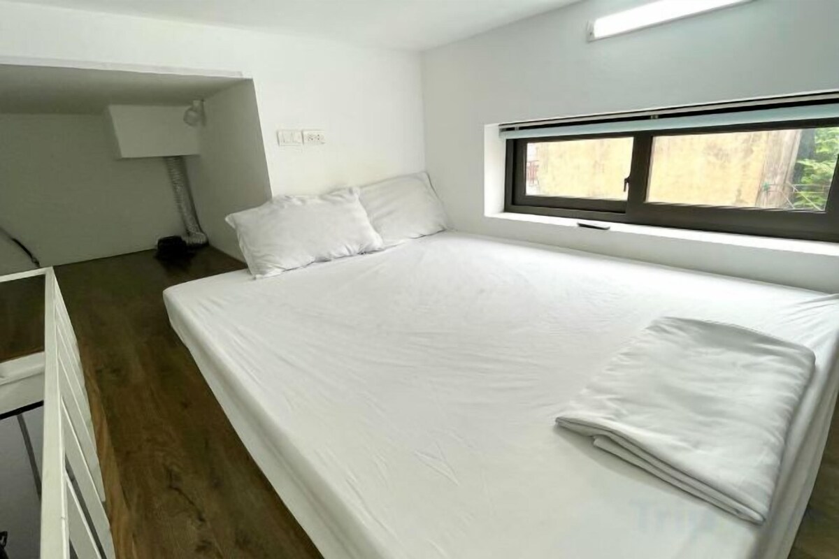 A single-bed room with a wooden floor, a window, and a bedside table with a lamp.
