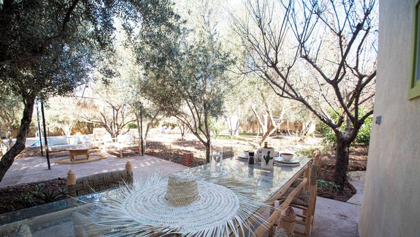 An outdoor dining area with a glass table, wicker chairs, and a woven placemat.