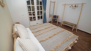 A room with a bed, a bench, a hanging clothes rack, and a door with curtains.