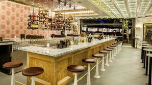 Eine Bar mit einer langen Theke, mehreren Hocker und einer Auswahl an Flaschen und Gläsern in Regalen.