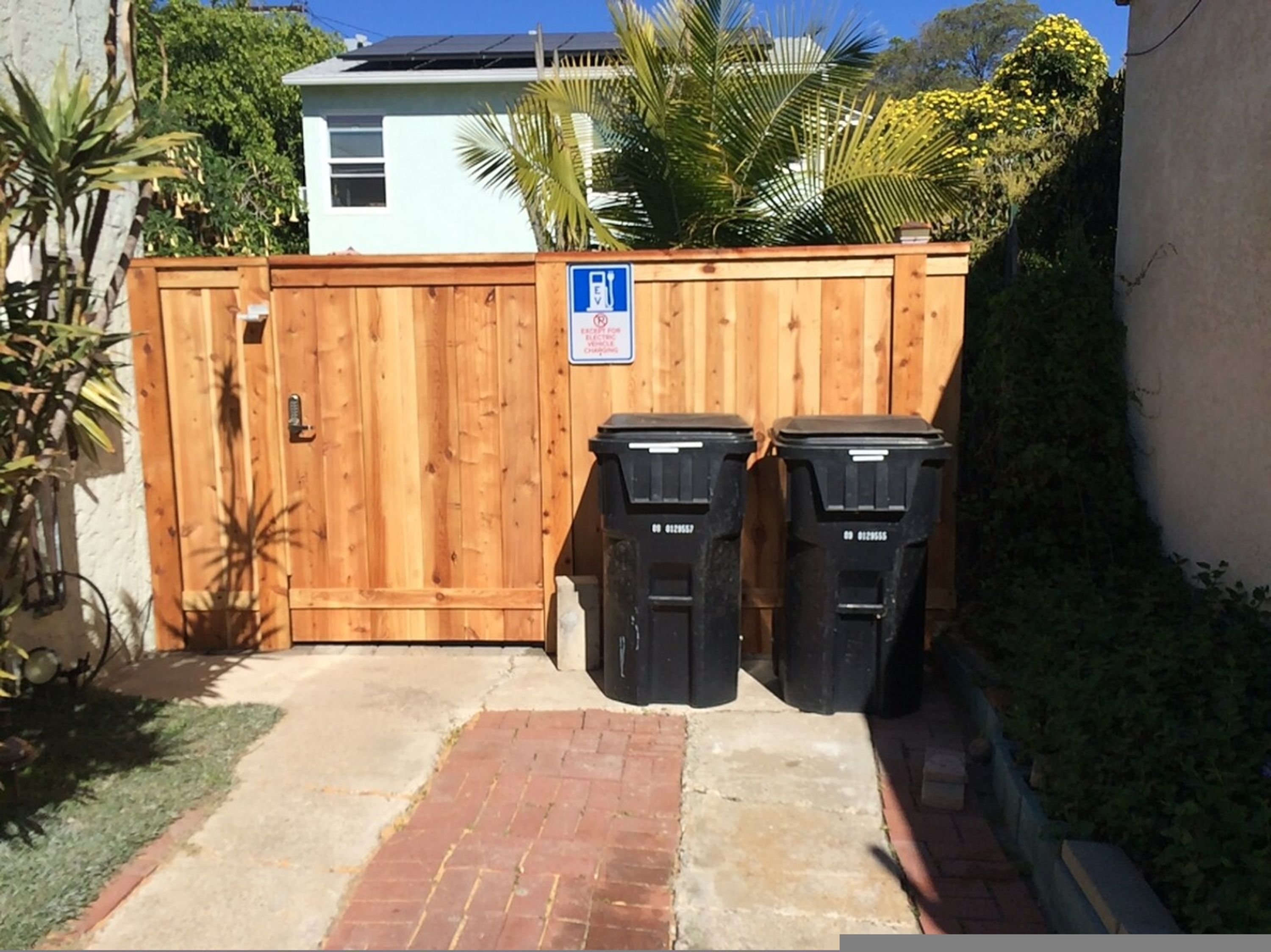 A wooden fence with two black trash bins in front.