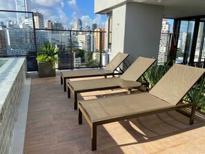 Een terras op het dak met lounge stoelen en een kleine plant in pot.