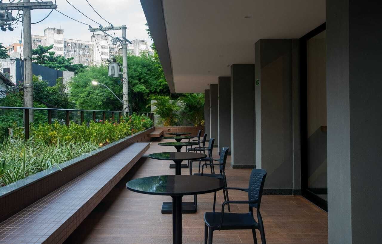 Uma área de estar moderna ao ar livre, com mesas e cadeiras, rodeada por vegetação e com vista para a cidade.