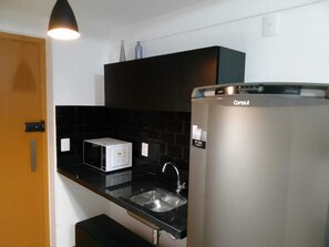 Compact kitchen with microwave, stainless steel refrigerator, and single sink.