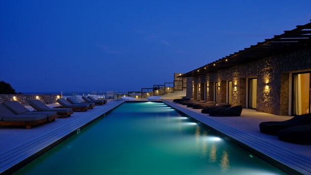 A poolside area with lounge chairs and a stone building with lights. - Villa Christy, Villa Christy (Mykonos)