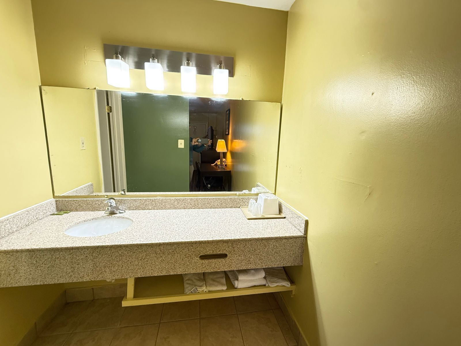Un baño con lavamanos de encimera de granito, un espejo con luces y un perchero para toallas.
