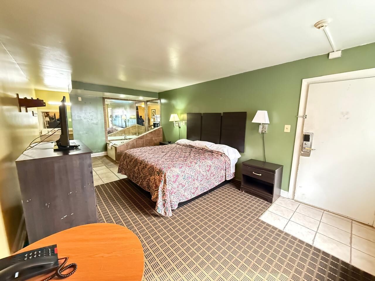 A hotel room with a bed, bedside table, lamp, and a desk with a telephone.