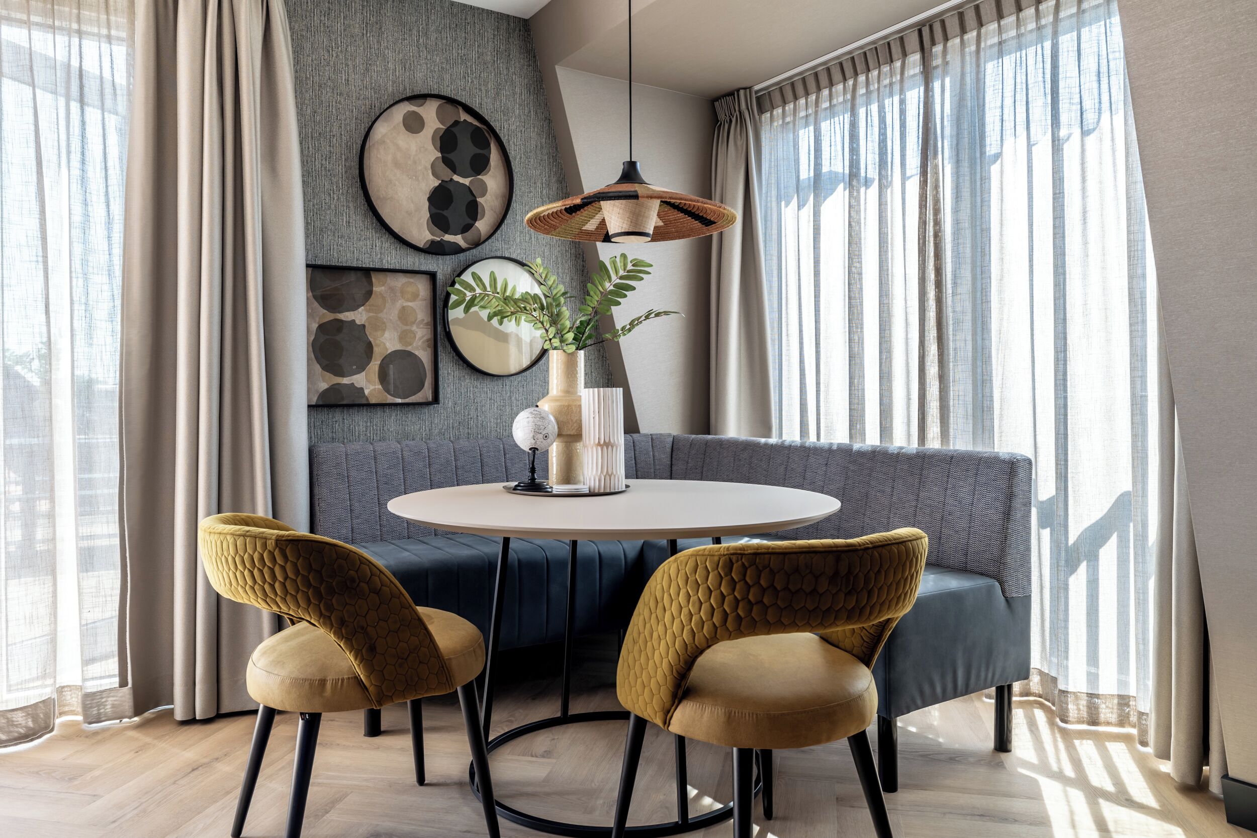 A modern dining area with a round table, two chairs, a hanging light fixture, and a blue sofa.