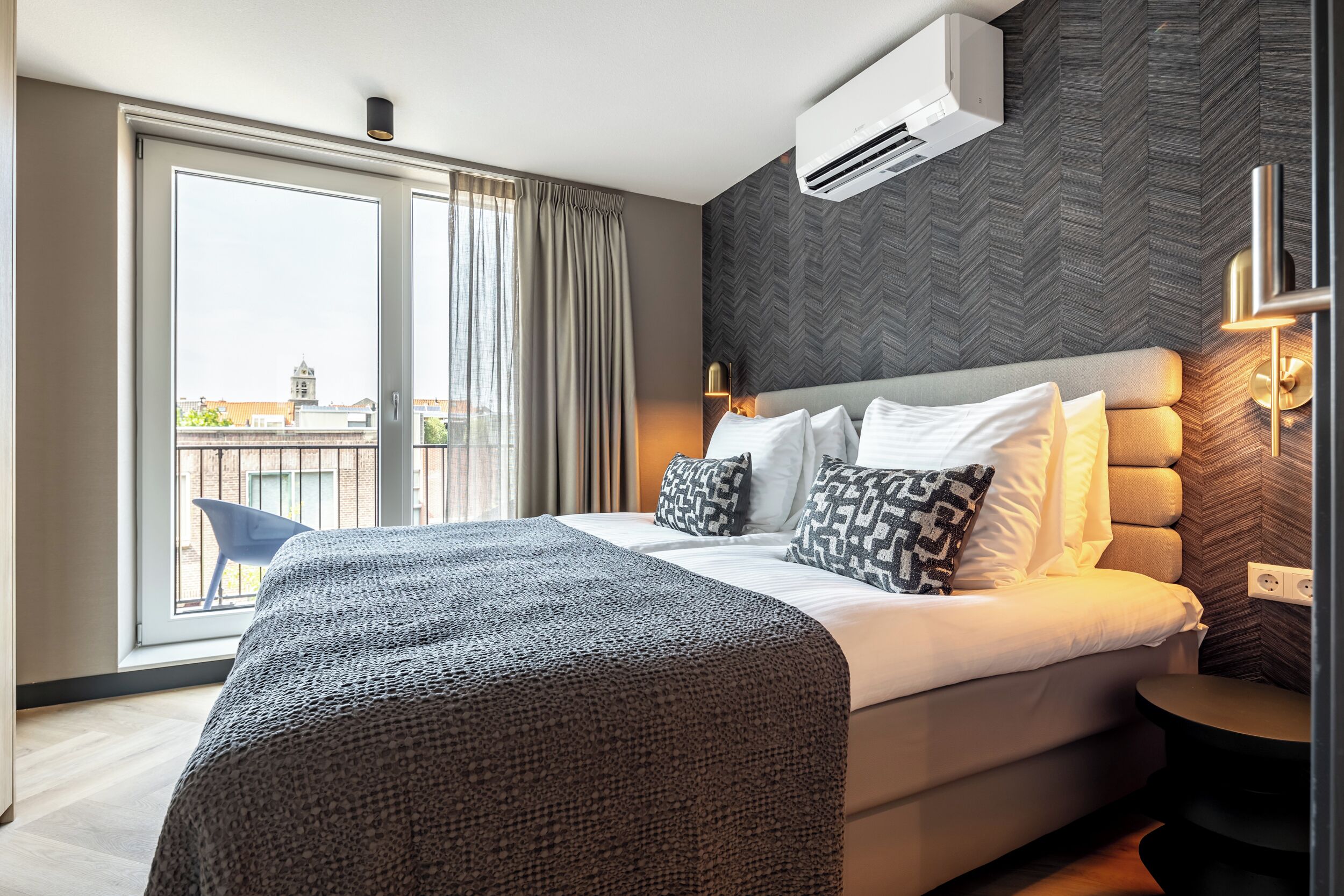 Una habitación de hotel moderna con una cama grande, vistas a la ciudad y un equipo de aire acondicionado.