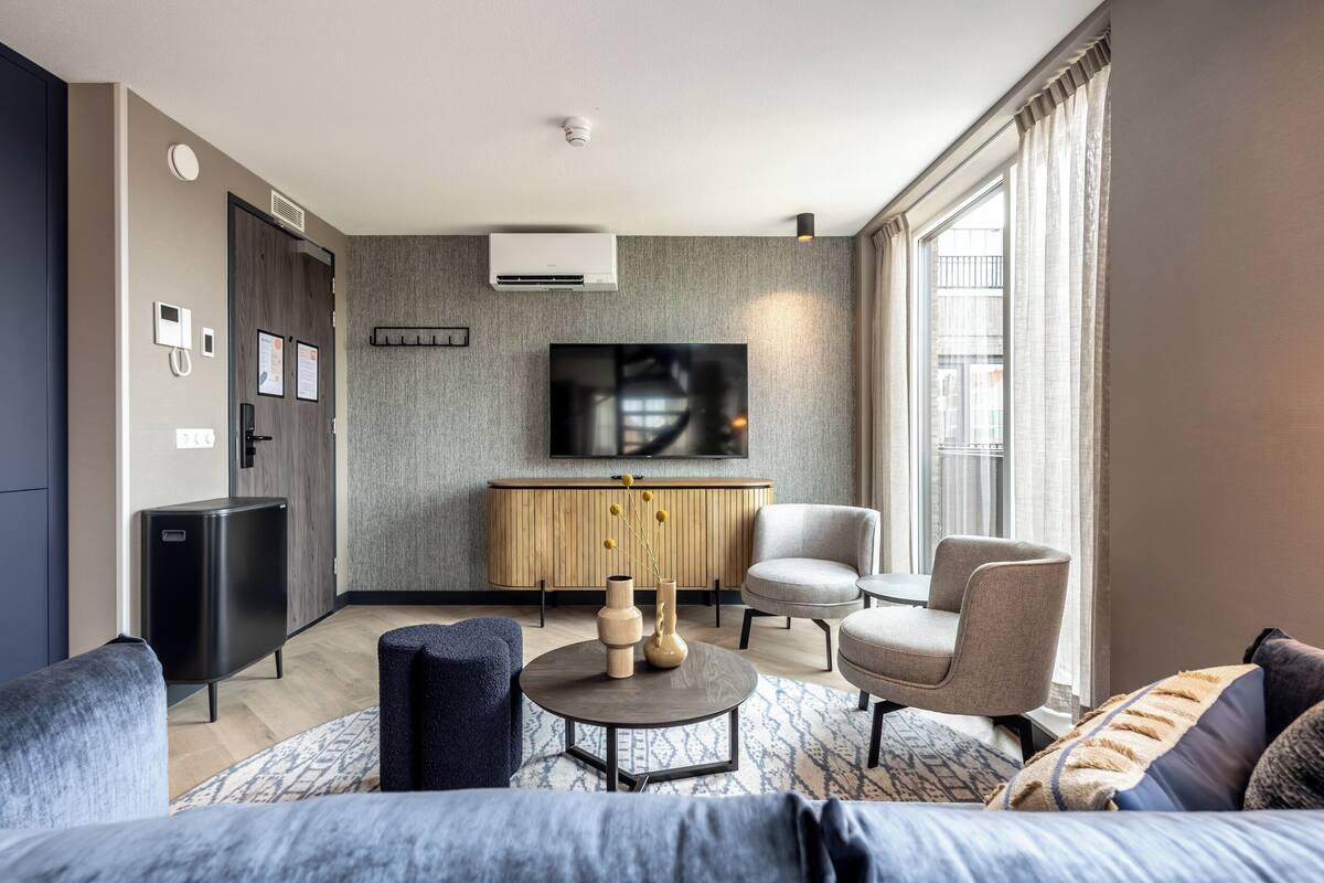 Ein modernes Wohnzimmer mit einer Couch, Sesseln, einem Couchtisch und einem Fernseher auf einer Holzkommode.