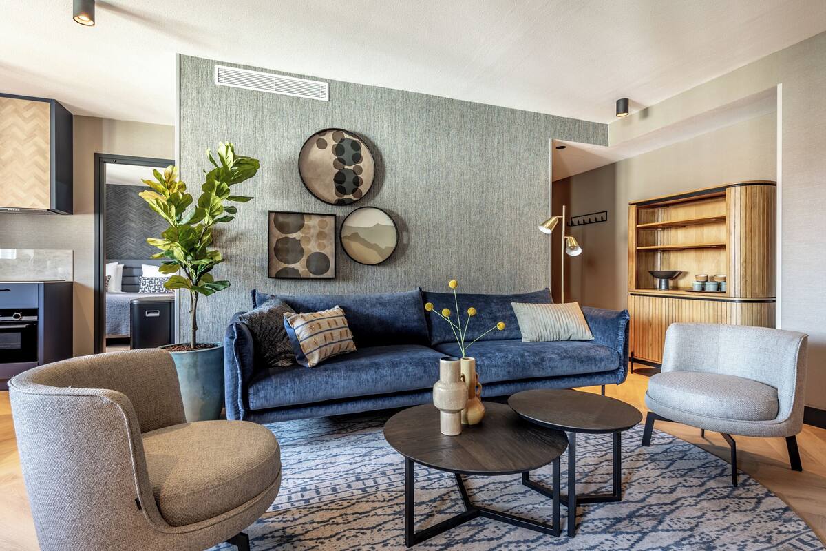 Ein modernes Wohnzimmer mit einem blauen Sofa, zwei Sesseln, einem Couchtisch und einer großen Topfpflanze.