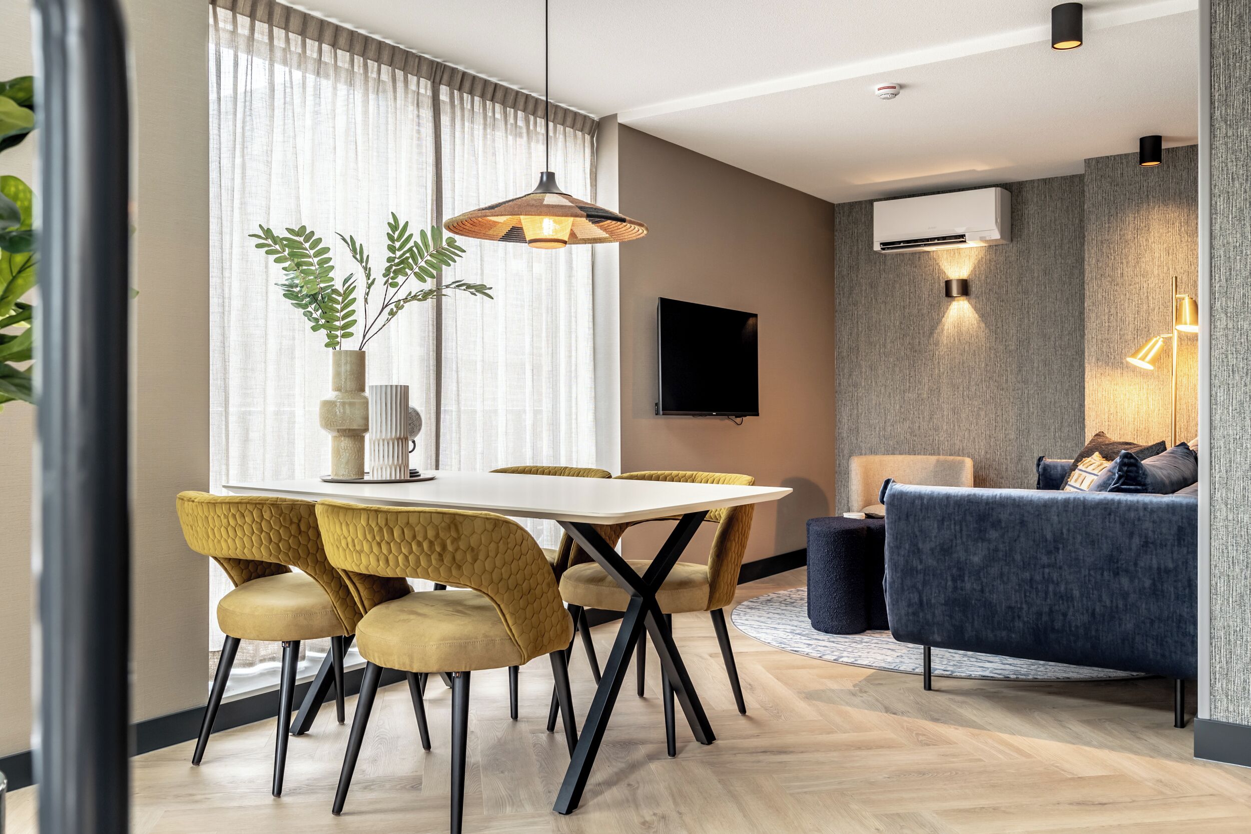 A modern living room with a sofa, a dining table with chairs, and a TV mounted on the wall.