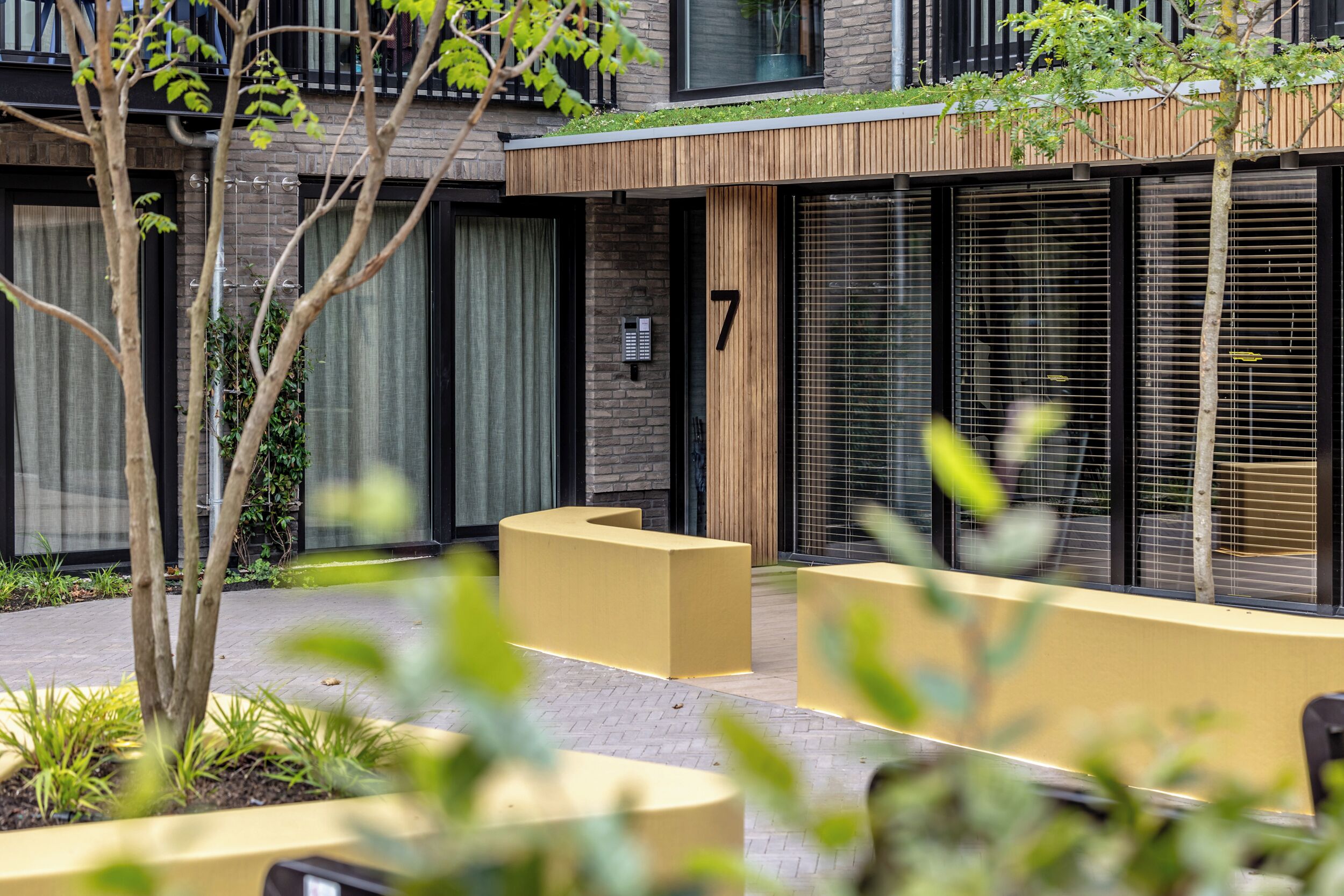 Un bâtiment moderne, orné d’un numéro 7, doté de grandes fenêtres et d’espaces extérieurs aménagés pour s’asseoir.