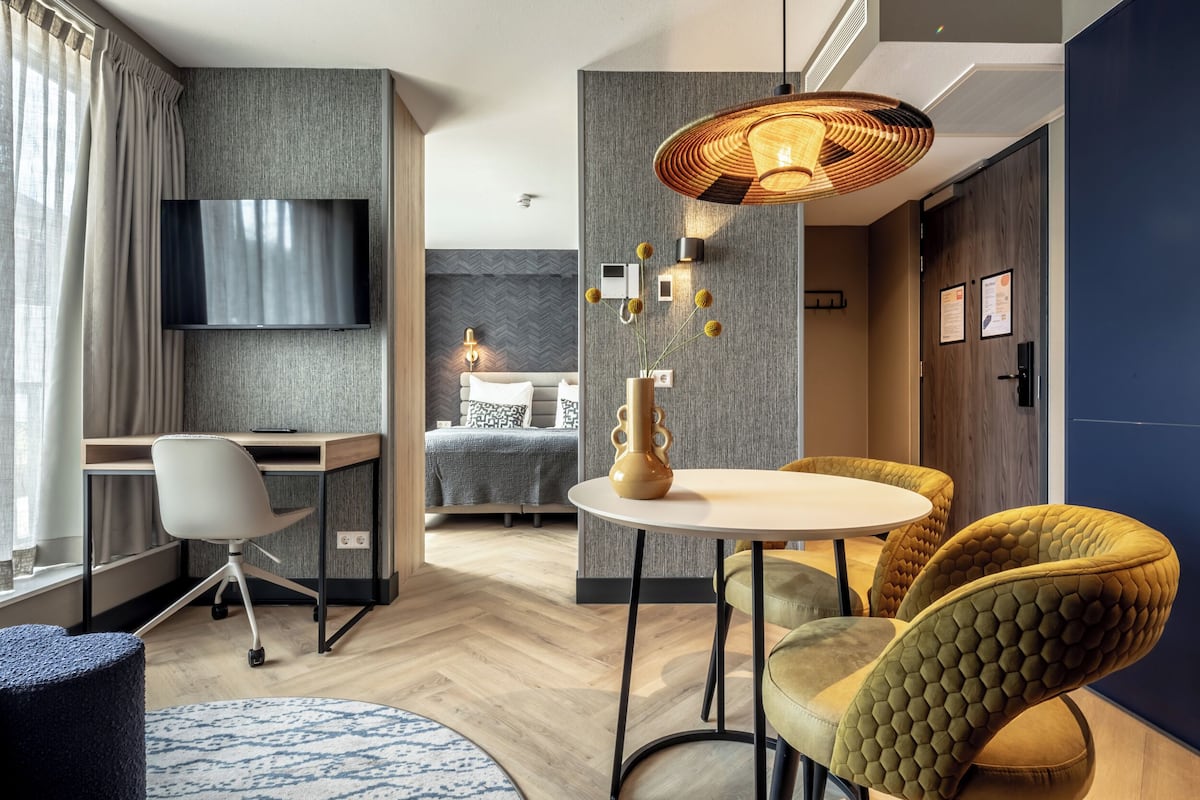 Ein modernes Hotelzimmer mit Schreibtisch, Stuhl, Bett und einer Essecke mit Sitzgelegenheiten.