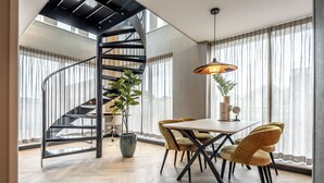 A modern interior with a spiral staircase, a dining area with a table and chairs, and large windows with sheer curtains. - BizStay Delft  (Delft)