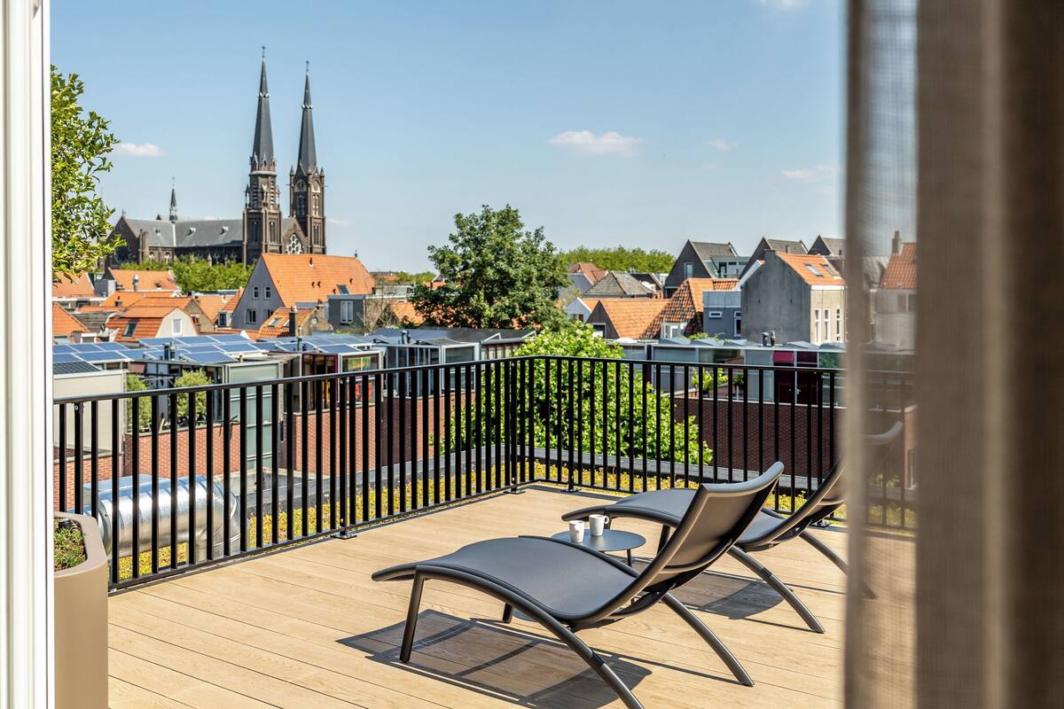 Ein Balkon mit zwei Stühlen und einem Tisch, mit Blick auf eine Stadt mit historischen Gebäuden und einer Kirche.