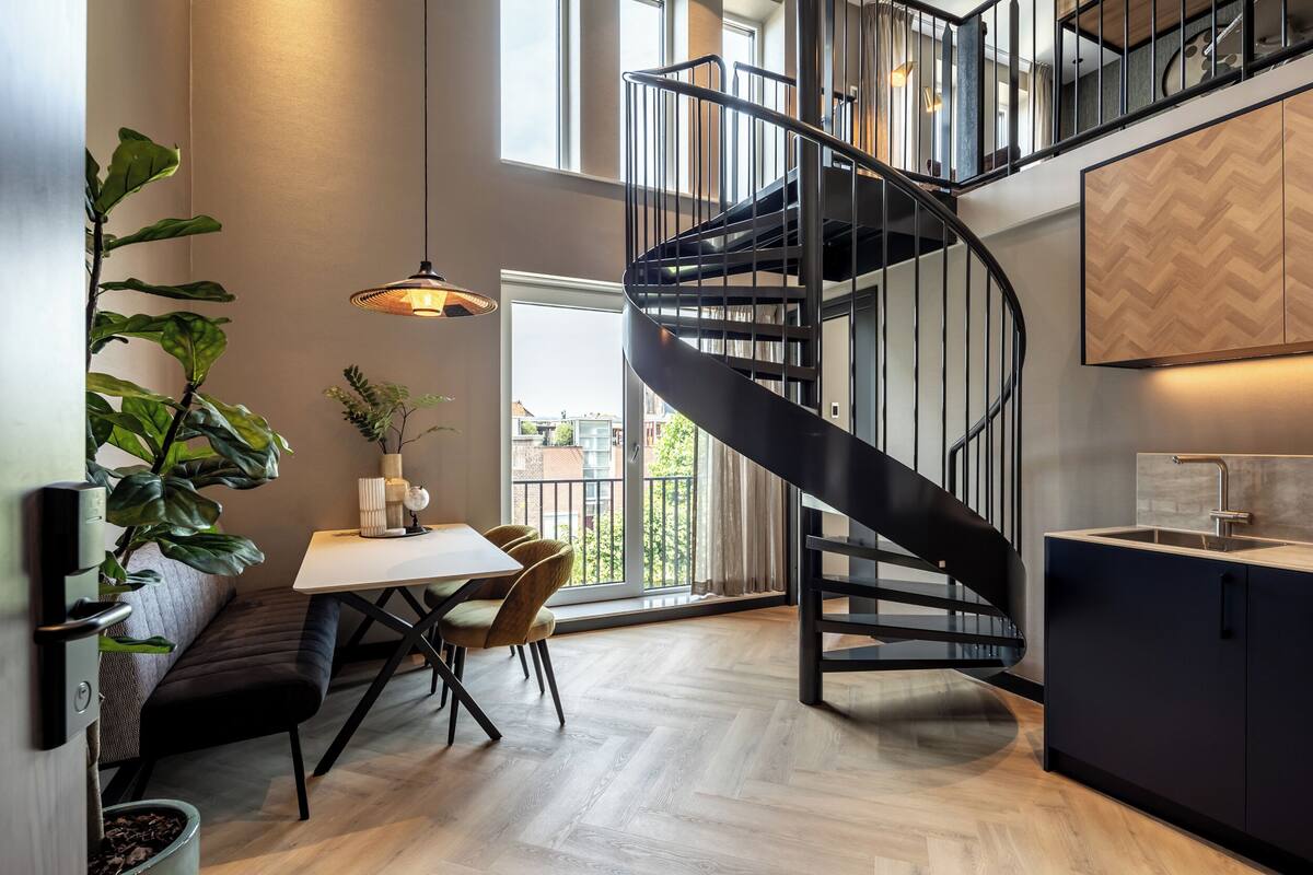 Eine moderne Küche mit einer schwarzen Wendeltreppe, Holzböden und einem Essbereich mit einer Bank und Stühlen.