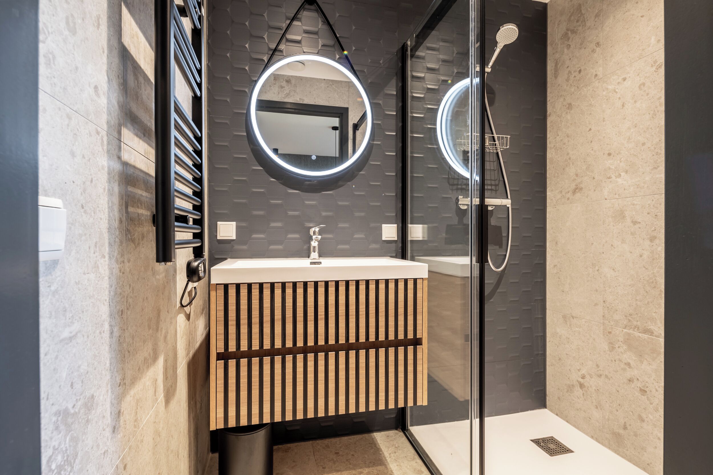 A modern bathroom with a glass shower enclosure, a wooden vanity with a mirror, and a tiled backsplash.