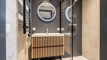 A modern bathroom with a glass shower enclosure, a wooden vanity with a mirror, and a tiled backsplash.