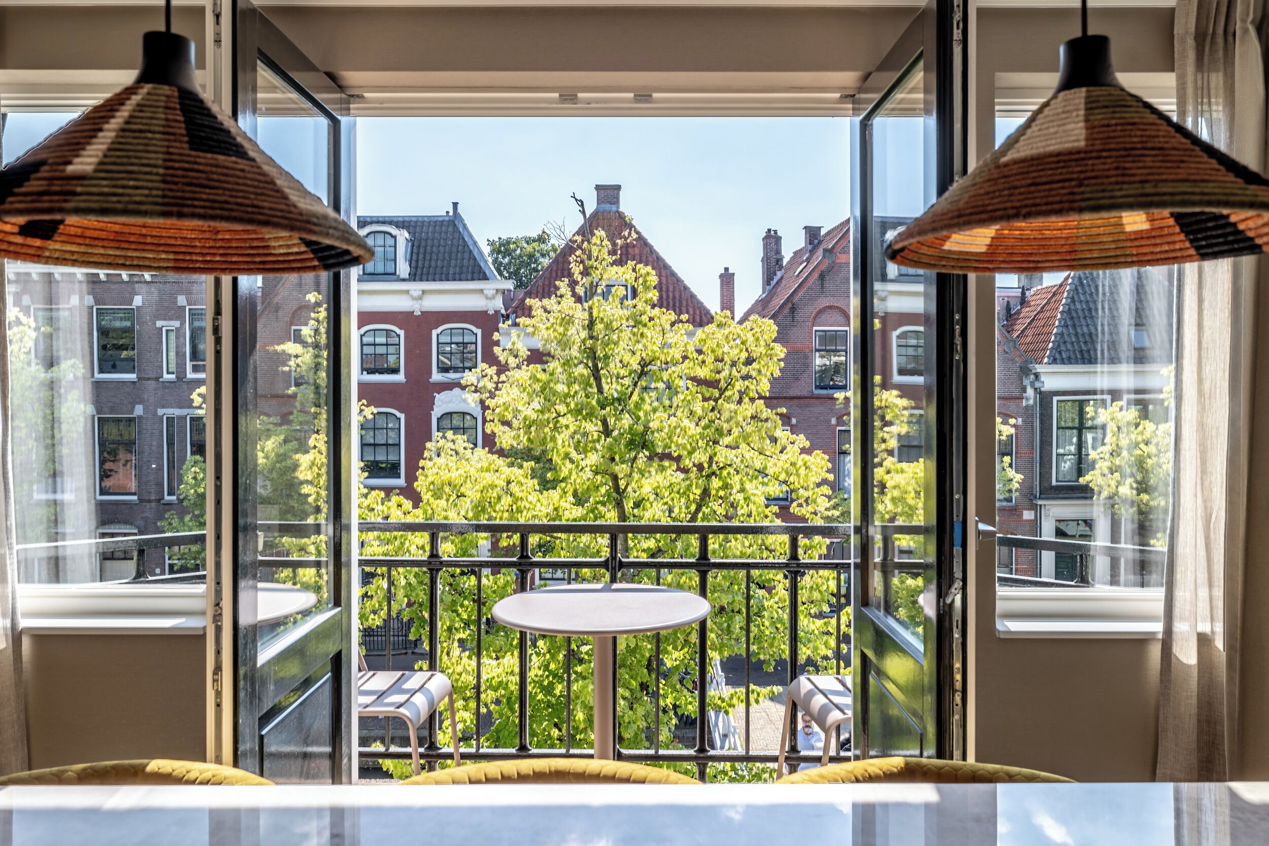 A room with a large window overlooking a tree and buildings. There is a round table and two chairs in the foreground. - BizStay Delft  (Delft)