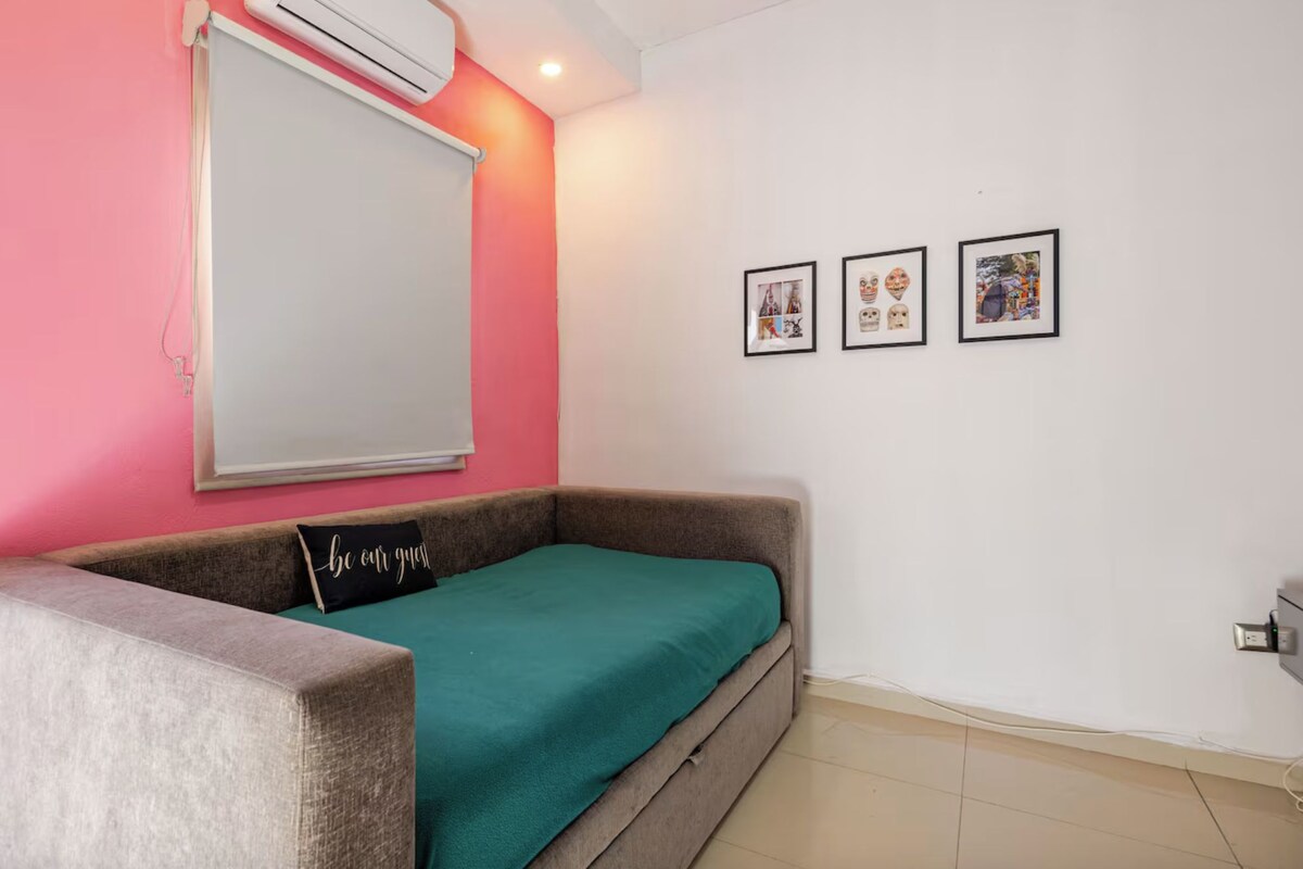 A small, cozy room with a single bed, a window with a white blind, and three framed pictures on the wall.